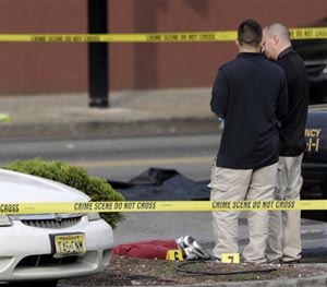 A person lays on the ground near evidence markers as officials investigate the scene where a Jersey City Police Department officer was shot and killed while responding to a call at a 24-hour pharmacy, Sunday, July 13, 2014, in Jersey City, N.J. (AP Image)