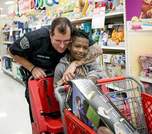 In this Dec. 15, 2016 file photo, Austin Police officer David Easley puts a tattooed arm around Jarvis Moblin, 8, in a hug during the 14th annual Shop With A Cop shopping spree at a Target in Austin, Texas.