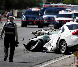 A crime scene investigator walks by a wrecked car involved in a school bus crash. (AP Photo/John Locher)