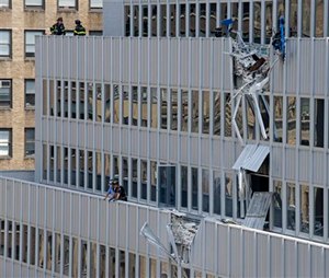 New York City firefighters stand near the damaged facade of 261 Madison Ave. after a piece of mechanical equipment being lifted by a crane broke free and fell about 28 stories to the sidewalk below, Sunday, May 31, 2015, in New York. Ten people including two construction workers were injured, but none of the injuries was considered life-threatening. (AP Photo/Craig Ruttle)
