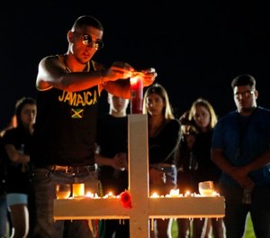 Joey Kandil, 18, a recent graduate of Marjory Stoneman Douglas High School, places a ring around a candle on one of seventeen crosses, after a candlelight vigil for the victims of the Wednesday shooting at the school, in Parkland, Fla., Thursday, Feb. 15, 2018. (AP Photo/Gerald Herbert)