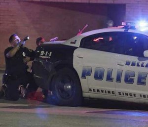 Dallas Police crouch behind a police car with their guns pointed toward a sniper.