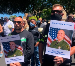 Matthew Rose, left, and Michael Carr, of Santa Cruz County hold posters of slain Sgt. Damon Gutzwiller, as they join others outside the Santa Cruz County Sheriff-Coroner's Office to pay their respects in Santa Cruz, Calif., Sunday, June 7, 2020. (AP Photo/Martha Mendoza)