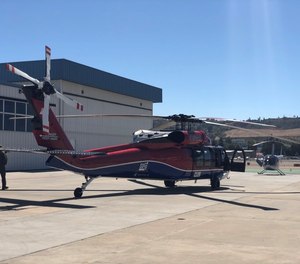 Two UH-60 Black Hawk helicopter equipped with aerial water buckets depart to support fire suppression during a wildfire.