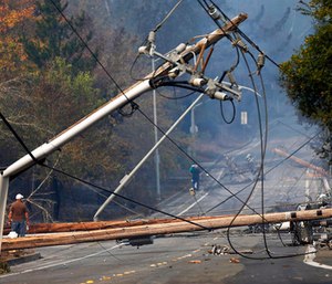 People walk past a fallen transformer and downed power lines on Parker Hill Road in Santa Rosa, Calif.