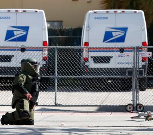 A member of the Miami-Dade County Police Bomb Squad looks for pieces of a suspicious package that was rendered safe after the bomb squad detonated the package that was found by a U.S. Postal employee who noticed what appeared to be wires coming out of an envelope at a post office, Monday, Nov. 5, 2018, in Miami Beach, Fla. (AP Photo/Wilfredo Lee)