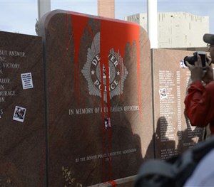 In this photograph taken Saturday, Feb. 14, 2015, protesters take pictures of red paint that was thrown on the memorial to fallen officers in Denver.