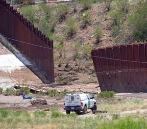 A border patrol vehicle stands guard at a section of collapsed fence just west of the Mariposa Port of Entry in Nogales, Ariz., Sunday, July 27, 2014, after severe storms in southern Arizona over the weekend knocked down a chunk of the metal border fence that divides Mexico and the U.S. Rain runoff from the storms destroyed about 60 feet worth of fence and caused damage to homes just north of it.