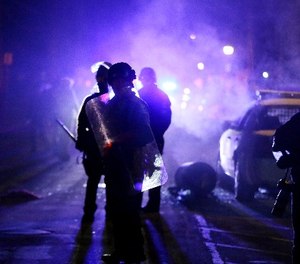 In this Nov. 25, 2014 file photo, police officers watch protesters as smoke fills the streets in Ferguson, Mo.