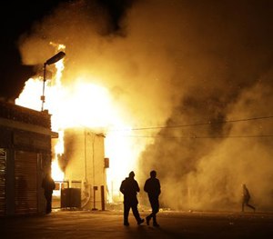 In this Monday Nov. 24, 2014 file photo, people walk away from a storage facility on fire after the grand jury decision was announced in Ferguson, Mo.