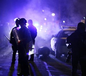 In this Nov. 25, 2014 file photo, police officers watch protesters as smoke fills the streets in Ferguson, Mo.