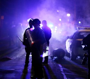 In this Nov. 25, 2014 file photo, police officers watch protesters as smoke fills the streets in Ferguson, Mo.