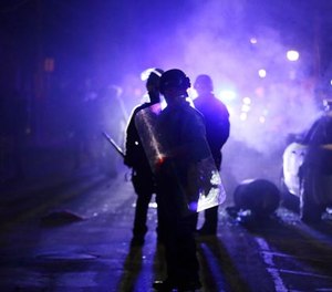 In this Nov. 25, 2014 file photo, police officers watch protesters as smoke fills the streets in Ferguson, Mo.