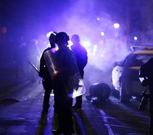 In this Nov. 25, 2014 file photo, police officers watch protesters as smoke fills the streets in Ferguson, Mo.