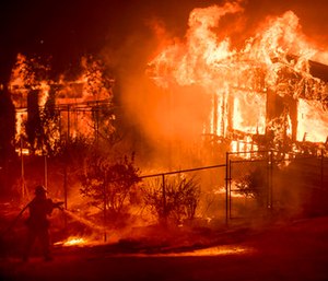 A firefighter sprays water as flames from a wildfire consume a residence near Oroville, Calif.