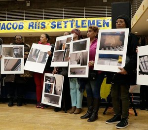 Residents of the Jacob Riis Settlement in New York City hold photographs of leaks, mold, peeling paint and other issues during a community town hall meeting on March 7, 2019.