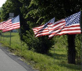 In this Thursday, May 30, 2013, photo, United States flags line the route of the funeral procession of Bardstown, Ky. Officer Jason Ellis during his funeral service. (AP Image)