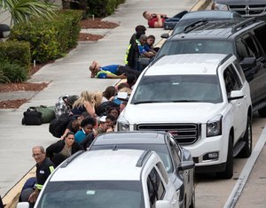 People take cover outside Fort Lauderdale–Hollywood International Airport, Friday, Jan. 6, 2017, in Fort Lauderdale, Fla., after a shooter opened fire inside a terminal of the airport, killing several people and wounding others before being taken into custody. (AP Photo/Wilfredo Lee)