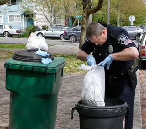Seattle Police officer Aaron Stoltz searches garbage and recycling bins, Friday, April 15, 2016, after human remains were found in a nearby container in Seattle.