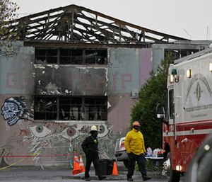 Fire officials walk past the remains of the Ghost Ship warehouse damaged from a deadly fire in Oakland, Calif.