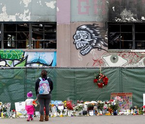 Flowers, pictures, signs and candles, are placed at the scene of a warehouse fire in Oakland, Calif.