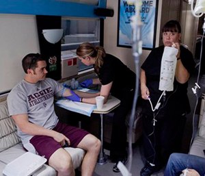 Emergency medical technician Debra Lund, right, prepares to hang an IV bag as co-worker Stacey Kreitlow, center, inserts an IV catheter into the arm of a patient.