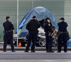 In this March 1, 2016 file photo, San Francisco police officers wait while homeless people collect their belongings in San Francisco.