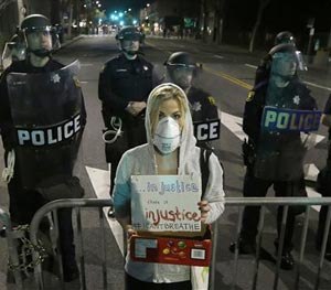 University of California Berkeley school of law graduated Alyson Reimer holds up a sign as she protests in response to police killings in Missouri and New York as Berkeley Police officers block a street in front of the police station in Berkeley, Calif., Monday, Dec. 8, 2014. (AP Image)