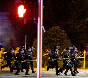 Police and Kentucky National Guard troops chase protesters as they flee toward a fence Sunday, May 31, 2020, in a parking lot at the corner of East Broadway and South Brook Street in downtown Louisville, Kentucky. (Max Gersh/The Courier Journal via AP)