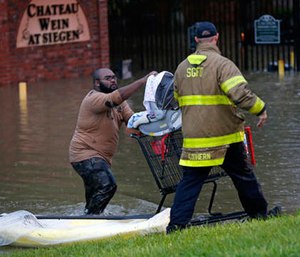 A member of the St. George Fire Department assists residents as they wade through floodwaters from heavy rains in the Chateau Wein Apartments in Baton Rouge, La., Friday, Aug. 12, 2016.
