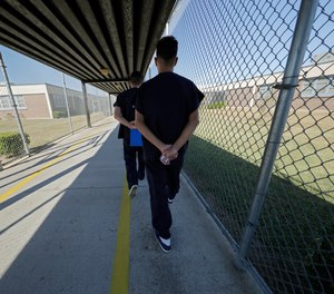 Detainees walk with their hands clasped behind their backs along a line painted on a walkway inside the Winn Correctional Center in Winnfield, La., Thursday, Sept. 26, 2019.
