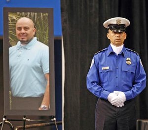 In this Nov. 12, 2013 file photo, a Transportation Security Administration officer stands in front of a portrait of slain TSA officer Gerardo Hernandez during his public memorial at the Los Angeles Sports Arena. (Al Seib/Los Angeles Times via AP Pool, File)