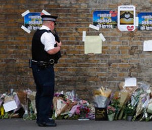 A police officer stands near floral tributes in Finsbury Park after an incident where a van struck pedestrians.