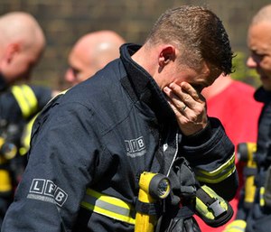 A firefighter puts his hand to his face as he looks at the floral tributes before a minute's silence near to Grenfell Tower.