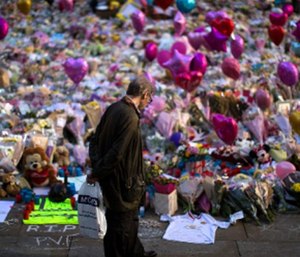 A man stands next to flowers for the victims of the bombing at St Ann's Square in central Manchester, England, Friday, May 26 2017.