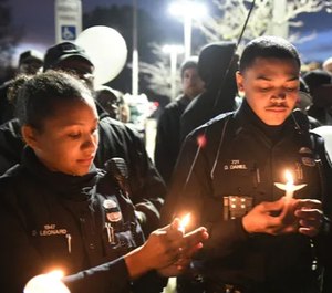 Detroit police officer Devon Leonard, left, relights the candle held by fellow officer Derrick Daniel, right, at a vigil for officer Rasheen McClain Monday night. (Photo/TNS)