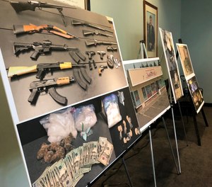 Photos of guns, drugs, and money are displayed at a news conference, Wednesday, Oct. 2, 2019, in Portland, Ore. (AP Photo/Gillian Flaccus)