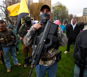 A protester carries his rifle at the State Capitol in Lansing, Mich., Thursday, April 30, 2020.
