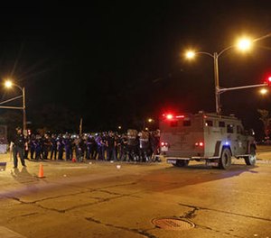 Police hide behind an armored vehicle as rocks are hurled at them in Milwaukee, Sunday, Aug. 14, 2016.