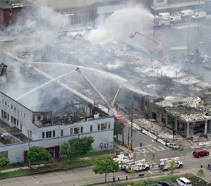 Firefighters work on an apartment building under construction, Thursday, May 28, 2020, tentatively known as Midtown Corner, left, after it was burned to the ground in Minneapolis, Minn. during protests. (Brian Peterson/Star Tribune via AP)