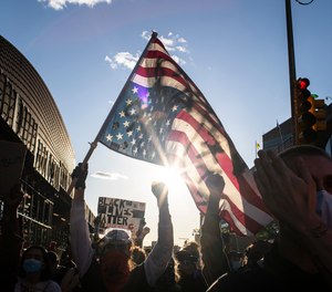 A man holds a U.S. flag upside down, a sign of distress, as protesters march down the street during a solidarity rally for George Floyd, Sunday, May 31, 2020, in the Brooklyn borough of New York.