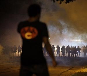 A man watches as police walk through a cloud of smoke during a clash with protesters Wednesday, Aug. 13, 2014, in Ferguson, Mo.