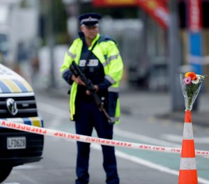Flower rest at a road block, as a Police officer stands guard near the Linwood mosque, site of one of the mass shootings at two mosques in Christchurch, New Zealand, Saturday, March 16, 2019.