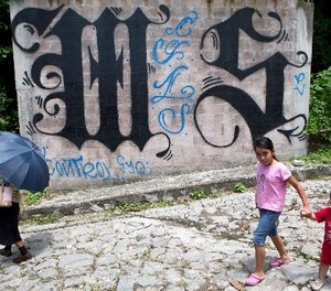 In this Aug. 21, 2014 file photo, a family walks by a wall covered by a symbol from the Mara Salvatrucha, of MS-13 gang in Ilopango, El Salvador. (AP Photo/Esteban Felix, File)