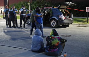 Two people walk past as police guard an SUV wherein a 3-year-old boy was fatally shot while riding in the vehicle with his father. Image: John J. Kim/Chicago Tribune via AP