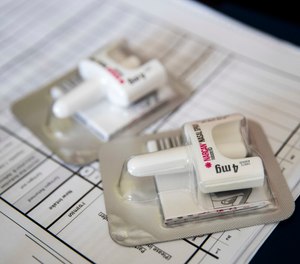 In this Tuesday, July 3, 2018, photo, a Narcan nasal device, which delivers naloxone, lies on a counter as VOCAL-NY health educator and naloxone coordinator Laura Levine gives a volunteer instructions on how to administer it at the organization's headquarters in the Brooklyn borough of New York.