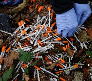 In this Nov. 8, 2017, file photo, a volunteer cleans up needles used for drug injection that were found at a homeless encampment in Everett, Wash.