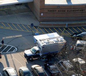 In this Dec. 14, 2012, file photo, officials stand outside of Sandy Hook Elementary School in Newtown, Conn., where authorities say gunman Adam Lanza opened fire inside school killing 20 first-graders and six educators at the school, and killed himself as police arrived. (AP Photo/Julio Cortez, File)