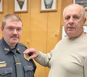 The new police chief for New York Mills, Robert C. Frankland, left, gets his badge pinned on by outgoing chief Donald Wolanin. (Photo/New York Mills Police Department)