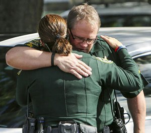 Law enforcement officers hug as other officers, not seen, escort the body of the Orange County deputy that died in the line of duty on Monday to the Orange County Medical Examiner's Office on Monday, Jan. 9, 2017, in Orlando, Fla. (Jacob Langston/Orlando Sentinel via AP)